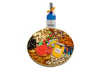 A round gourmet gift platter filled with assorted nuts, dried fruits, candies, and a small bottle of wine, isolated on a white background.