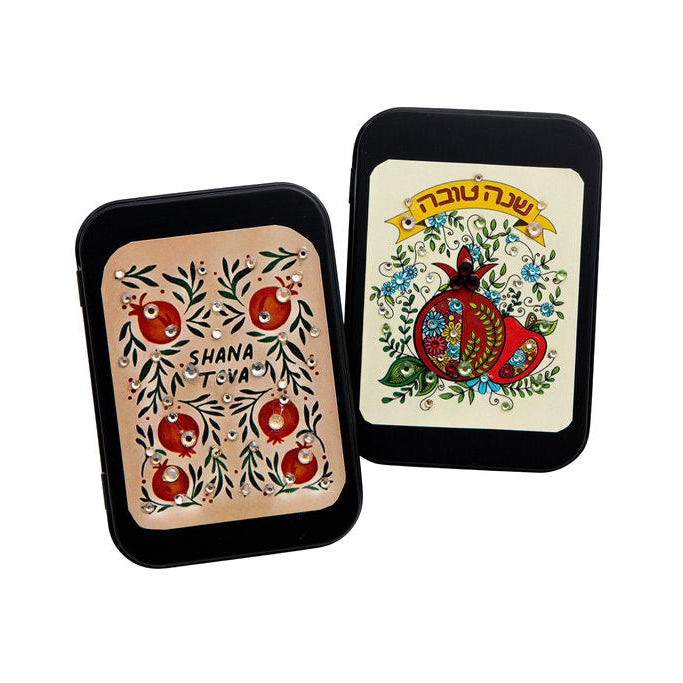 Two small rectangular matchboxes with rounded corners, shown on a white background. One case has a beige insert with red pomegranate illustrations and the text 'Shana Tova'