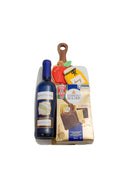 A gift basket containing a bottle of Bartenura wine, a bag of Ferrero Rocher chocolate, and a small wooden cutting board with a decorative apple and honey-shaped cookies, set against a plain white background.