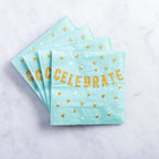 Turquoise napkins with gold 'CELEBRATE' text and confetti on a light gray background