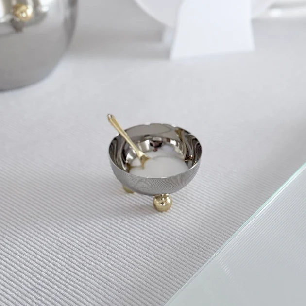 Small metallic bowl with a spoon on a textured white surface